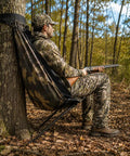 Hunter using low profile hunting chair hammock seat with 360 degree swivel, camouflage for deer and turkey hunts in forest