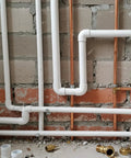 PVC pipes with fittings installed on a brick wall in a construction setting, featuring 2 Inch PVC End Cap For Schedule 40 Pipe, White Slip Socket.