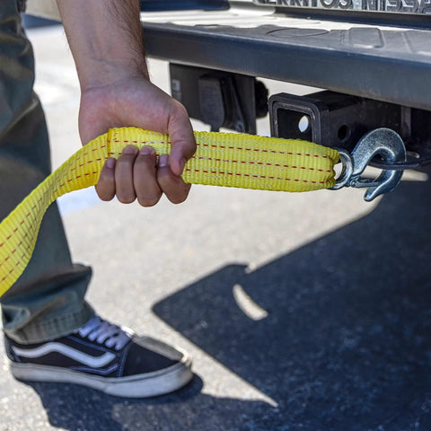 Person attaching Heavy Duty Tow Strap With Hooks, 2 Inch By 20 Foot, 10,000 Pound Capacity, Bright Yellow Polyester Webbing to a vehicle.