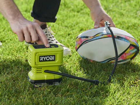 18V One Plus Cordless Tire And Ball Inflator With Mini Compressor 11 Bar Max Fast Inflation To 32 PSI In Under A Minute Includes 3 Tips Battery Not Included shown inflating a rugby ball on grass.