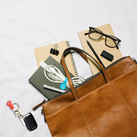 Image showing a brown leather bag with notebooks, glasses, and white cables organized with a Magnetic Cable Clips Set Of 12 for Cable Management and Organization Earbud Winder USB Cable Keeper Whiteboard And Fridge Magnet Clips Cord Wrap Ties for Laptops Desks and Home Office.