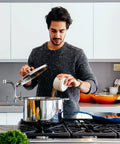 Person cooking in modern kitchen with stainless steel pot on stove.