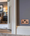 Modern Screwless Double Switched Wall Socket In Polished Copper Hella Easy Install Power Outlet For Home Renovation, mounted on a wall.