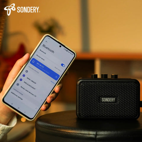 Ultra Portable 5W Mini Guitar Amp For Electric Guitars With Two Speakers And Rechargeable Battery beside smartphone showing Bluetooth.