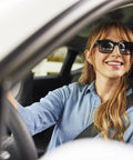Sunglasses on smiling woman driving a car; black frames, denim shirt, seat belt
