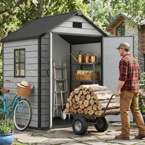 Man loading firewood into 6 By 4.4 Ft Backyard Storage Shed With Floor Durable 16mm Resin Construction Weatherproof Lockable Tool Shelter With Window And Vents For Bikes Lawn Gear Garden Tools Gray, with a blue bike and garden tools inside.