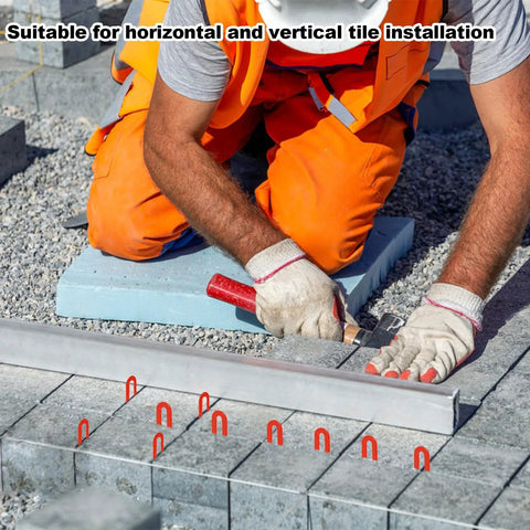 Front view of a construction worker kneeling with blue plastic horseshoe tile shims and red spacers used for leveling tiles.