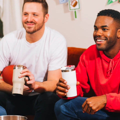 Two men enjoying drinks from 20oz Ceramic Lined Travel Tumblers With Double Wall Vacuum Insulation on a couch.