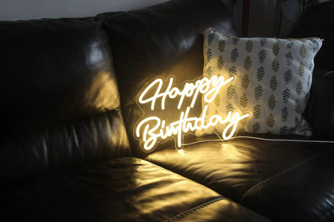 LED Neon Sign Night Light For Wall Decor And Party Vibe Perfect For Bedroom Living Room Bar Wedding Birthday Christmas USB Powered 5V Low Voltage Neon Sign With Easy Hang Chain Light Modulator 16.5 x 9.1 Inches, displaying 'Happy Birthday' on a leather sofa.