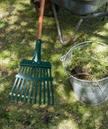 Heavy Duty 11-Tooth Carbon Steel Rake Head 10 Inch Wide Replacement With Pre Drilled Holes for lawn care next to a bucket of leaves