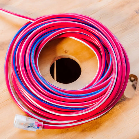 Coiled Beefy Built Tough Outdoor Extension Cord 50 Ft 12 Gauge 3 Conductor With Lighted End SJTW Contractor Grade on wooden surface.
