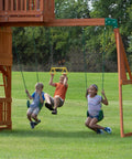 Children swinging on the Skyfort II Cedar Wood Swing Set With Wave Slide, Raised Clubhouse, monkey bars and trapeze.