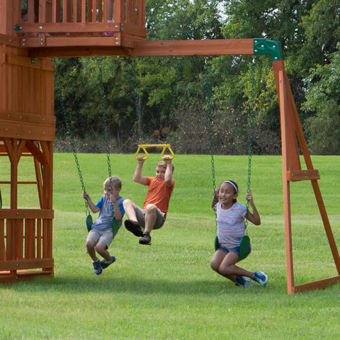 Children swinging on the Skyfort II Cedar Wood Swing Set With Wave Slide, Raised Clubhouse, monkey bars and trapeze.