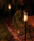 Metal Solar Torch Lights With Adjustable Height From 24 To 50 Inches For Outdoor Yard Patio And Garden Pathway Waterproof Tiki Torches In Matte Black Two Pack Featuring Patented LED Flame Effect And Realistic Flicker installed in garden pathway