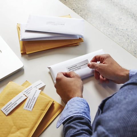 Person applying Hassle Free Direct Thermal Mailing Address Labels In Bright White, Sized 1-1/8 X 3-1/2 Inches to an envelope.