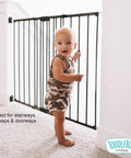 Baby standing by Easy Swing and Lock Baby Gate Series 2 Hardware Mounted Metal Safety for Stairs and Doorways Kid Safe Adjustable gate.