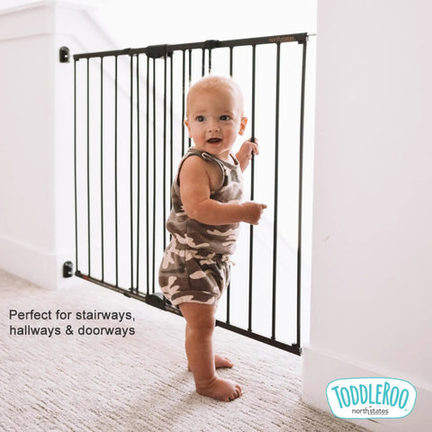Baby standing by Easy Swing and Lock Baby Gate Series 2 Hardware Mounted Metal Safety for Stairs and Doorways Kid Safe Adjustable gate.
