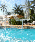 Adjustable Dual Spray Pool Fountain for Above Ground and In Ground Pools spraying water over a pool with palm trees in background
