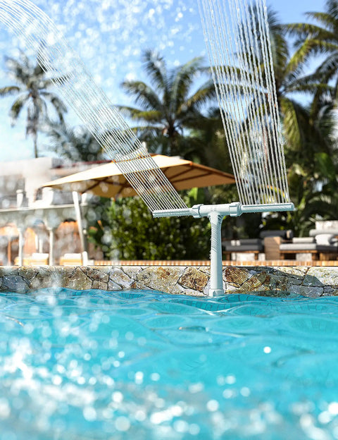 Adjustable Dual Spray Pool Fountain for Above Ground and In Ground Pools spraying water over a pool with palm trees in background