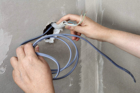 Hands installing cables through a wall opening with heavy duty floor grommet system for cable management and organization.