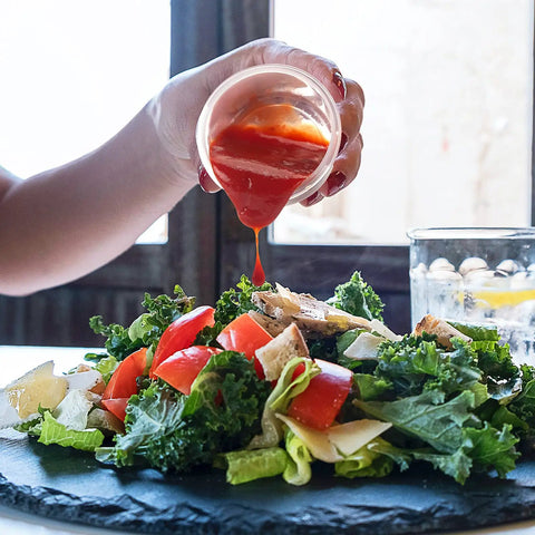 Pouring dressing from 2.7 oz condiment container onto salad, showcasing 6 Pack 2.7 Oz Condiment Containers With Leakproof Lids For Grab And Go Meals Reusable BPA Free Sauce Dishes Perfect For Lunch Boxes Dips Dressings And Sauces.