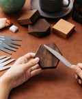 Sanding sticks set: close-up of hands sanding a hexagonal wooden block with a metal file, assorted sticks visible.