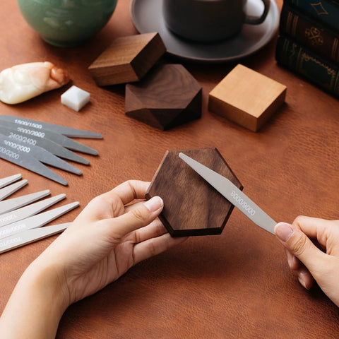 Sanding sticks set: close-up of hands sanding a hexagonal wooden block with a metal file, assorted sticks visible.