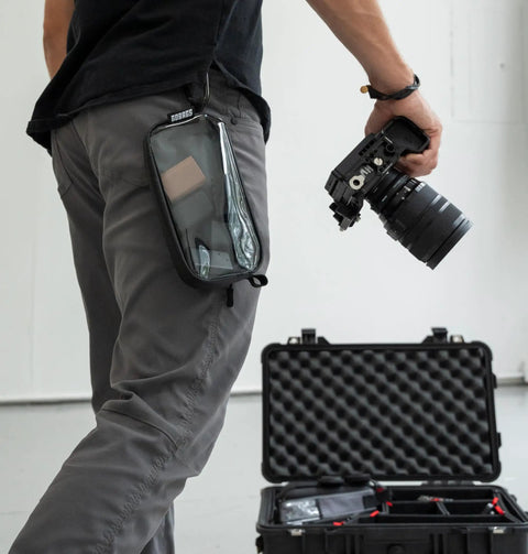Person holding camera with Neo Zipper Gear Organizer Bag For Electronics And Cameras Cable Organizer Pouch attached to pants.