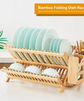 Heavy Duty Bamboo Dish Drying Rack Three Tier Collapsible Wooden Drainer With Utensil Holder holding plates and bowls on a kitchen counter.