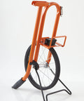 Measuring Wheel With Spoked Wheel And Metal Frame, Geared Mechanical Clicker Counter, Center Line Design, Feet Graduations, 11.5 Inch Diameter, Built Tough Three Quarter Inch Steel Frame, Dirt Shield Shelf, Bright Orange standing on stand.
