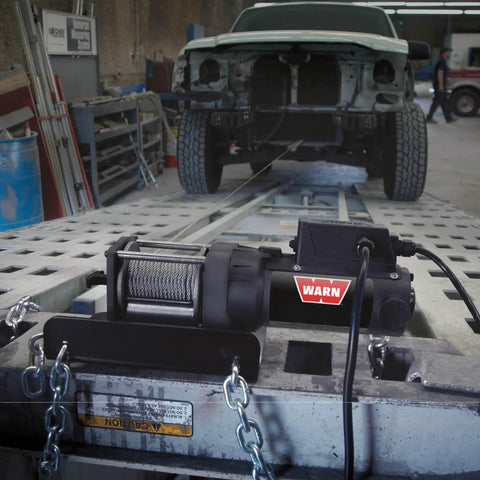2000 Lb 12V Electric Winch With Steel Cable, Hook And Corded Remote Portable Compact Power in a workshop with chains and vehicle