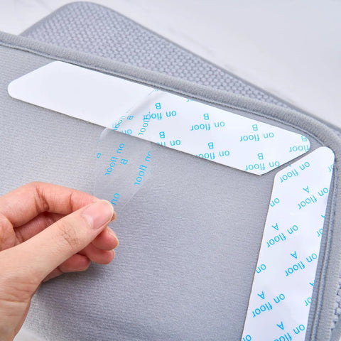 Close-up of hand peeling back adhesive layer on 8 Pack Washable Non Slip Rug Pads Double Sided For Floors Black Reusable Rug Grips