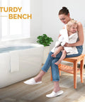 Woman sitting on Dope Bamboo Shower Bench Spa Stool With 2 Tier Wood Seat next to bathtub, holding child in bathroom.