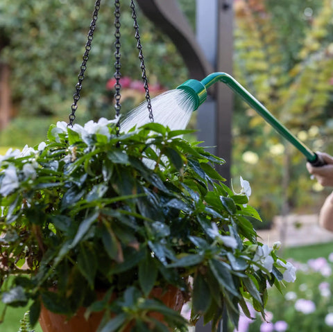 36 Inch Front Trigger Watering Wand Hose Nozzle With Carbon Fiber Texture And Non Slip Grip, Long Reach Garden Hose Sprayer For Precise Plant Watering And Flow Control in use watering hanging white flowers in garden.