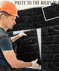 Installer applying Sleek Black 3D Wall Panels Peel And Stick Foam Brick Wallpaper Tiles on wall with adhesive, DIY decor.
