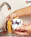White ceramic mug with pink "Tuesday" script being rinsed under a kitchen faucet; AIVA Paper Group logo in the corner.
