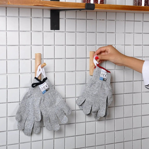 Two pairs of Food Grade Cut Resistant Gloves Level 5 Safety hanging on wall with hand adjusting, suitable for chefs and home use.