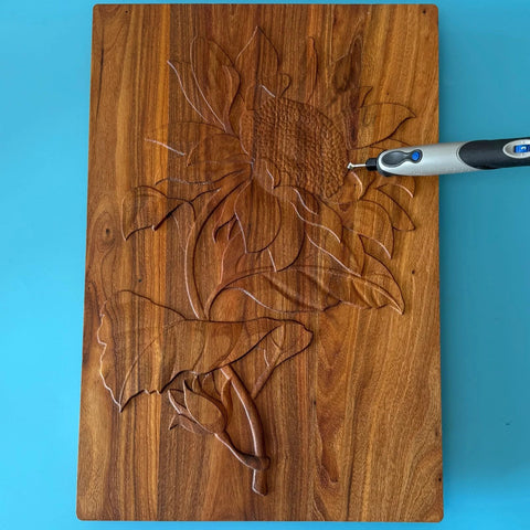 Dremel-style rotary tool with carbide burr carving a floral design into a wooden plaque.