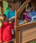 Children playing in Cedar Cove Wooden Swing Set With Spiral Tube Slide And Wave Slide, Elevated Clubhouse With Balcony, Toy Grill