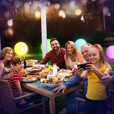 Family enjoying dinner outdoors with 16 Inch Light Up Glow Beach Ball With 8 LED Modes For Night Pool Fun, glowing in the background.