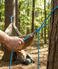Person using Six Pack Rope With Roller Tensioner Set For Easy Secure Tying Pro Grade Heavy Duty Retractable Buckle Rope in forest camp setup