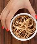 Top view of a hand holding a bowl of natural crepe rubber bands, 3.5x0.25 inches, for packaging use in warehouses and schools.