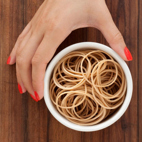 Top view of a hand holding a bowl of natural crepe rubber bands, 3.5x0.25 inches, for packaging use in warehouses and schools.