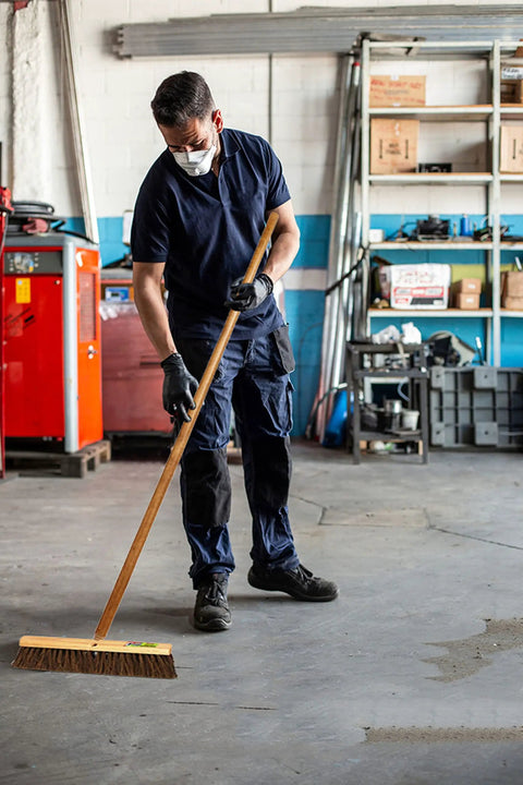 Man using Heavy Duty 18 Inch Palmyra Bristle Push Broom For Garage Indoor Floor Sweep on concrete floor.