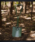 23 Inch Folding Camping Shovel With Cover High Manganese Steel Entrenching Tool resting in forest soil