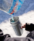 Person using Spot Spreader 80 Oz Handheld Grab-And-Go Dispenser for salt, showing open lid and strong handle in snowy environment.