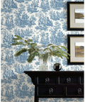 Country Life Toile Peel And Stick Wallpaper Roll For Easy DIY Accent Wall Blue And White No Water Needed Quick Peel And Stick Application 20.5 Inches Wide By 16.5 Feet Long 100 Percent Removable No Sticky Residue Renters Friendly decor with blue toile pattern behind a black table and glass vase with green ferns