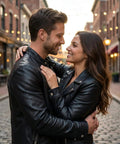 Couple in leather jackets embracing on a cobblestone street with string lights.