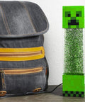 Glitter Creeper Mood Light 12 Inch LED Lamp for Gaming Rooms next to backpack, Minecraft themed night light with glitter glow