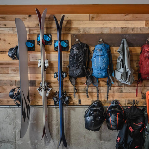 Badass Gravity Lock Ski And Snowboard Wall Storage Rack Holds 3 Pairs Damage Free Gear Saver With Anti Slip Pad Protects Tips Tails And Rockers For Safe Indoor Equipment Organization In Black with skis and backpacks on a wooden wall